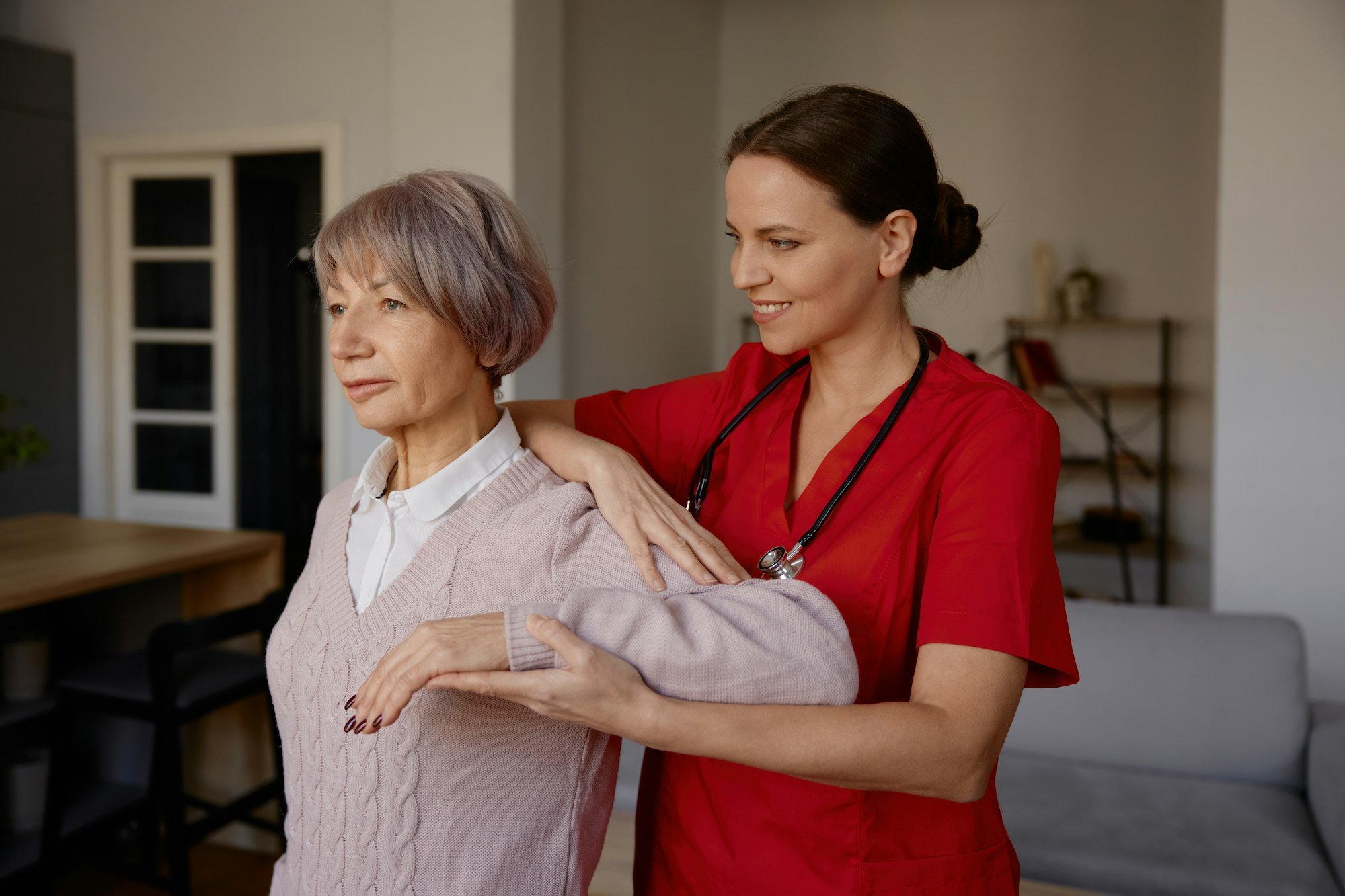 Woman rehabilitation therapist assisting senior female exercising at home